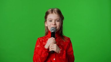 Çocuk duyguları reklam konsepti. Gülümseyen kız çocuğu karaoke mikrofonunda şarkı söylüyor, pozitif ifade, krom anahtar yeşil ekranda izole edilmiş arka plan modeli..