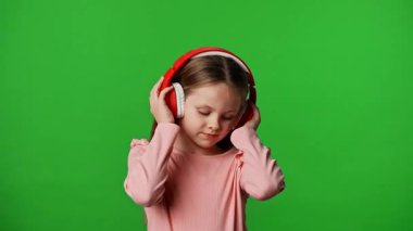 Çocuk duyguları reklam konsepti. Gülümseyen çocuk kulaklıkla müzik dinliyor ve dans ediyor, pozitif ifade, krom anahtar yeşil ekranda izole edilmiş arka plan modeli..