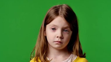 Çocuk duyguları reklam konsepti. Sarı tişörtlü küçük kız kameraya bakıyor, nötr bir ifade, krom anahtar yeşil ekranda izole edilmiş arka plan modeli..
