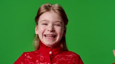 Çocuk duyguları reklam konsepti. Gülümseyen kız heyecanla el sallıyor ve gülüyor ve yüzünü tutuyor, olumlu ifade, krom anahtar yeşil ekran arka plan modelinde izole edilmiş..