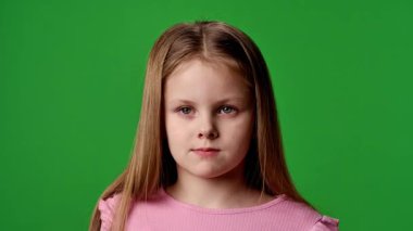 Çocuk duyguları reklam konsepti. Tişörtlü küçük kız kameraya bakıyor ve göz kırpıyor, nötr bir ifade, krom anahtar yeşil ekranda izole edilmiş arka plan modeli..