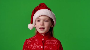 Çocuk duyguları reklam konsepti. Noel Baba şapkalı gülümseyen kız elleri ve gülücükler saçıyor, olumlu ifade, krom anahtar yeşil ekranda izole edilmiş arka plan modeli..