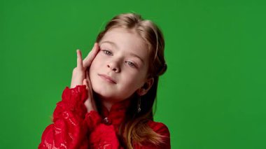 Çocuk duyguları reklam konsepti. Gülümseyen kız çocuğu kameraya poz veriyor, yüzlerine dokunuyor ve sevimli jestler yapıyor, olumlu ifade veriyor, krom anahtar yeşil ekran arka plan modelinde izole edilmiş..