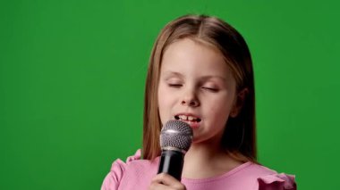 Çocuk duyguları reklam konsepti. Gülümseyen kız çocuğu karaoke mikrofonunda şarkı söylüyor, pozitif ifade, krom anahtar yeşil ekranda izole edilmiş arka plan modeli..