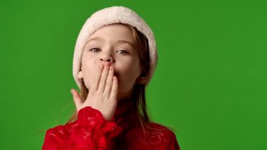 Çocuk duyguları reklam konsepti. Noel Baba şapkalı, gülümseyen bir kız çocuğu hava öpücüğü verir ve gülümser, olumlu ifade, krom anahtar yeşil ekran arka plan modelinde izole edilmiş..