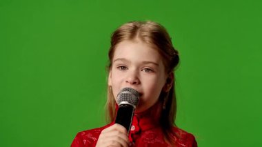 Çocuk duyguları reklam konsepti. Gülümseyen kız çocuğu karaoke mikrofonunda şarkı söylüyor, pozitif ifade, krom anahtar yeşil ekranda izole edilmiş arka plan modeli..
