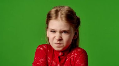 Çocuk duyguları reklam konsepti. Çapraz kollu ve kızgın yüzlü gülümseyen kız kameraya bakıyor, negatif yüz ifadesi, krom anahtar yeşil ekran arka plan modelinde izole edilmiş..