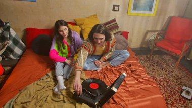 Genç bir kadın ve erkeğin eski bir gramofonla müzik dinlediği canlı bir sahne..