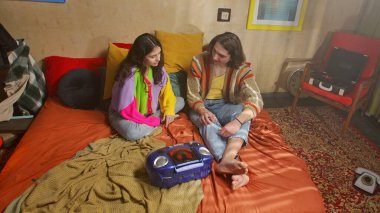 Genç bir kadın ve erkeğin eski bir kayıt cihazında müzik dinlediği canlı bir sahne..