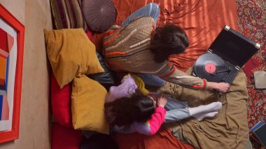 Genç bir kadın ve erkeğin eski bir gramofonla müzik dinlediği canlı bir sahne. Üst çekim