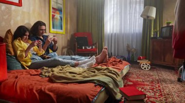 Bir çift renkli bir retro odasında rahat vakit geçirirken telefonlarıyla vakit geçiriyorlar..