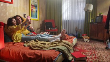 İki genç insan bir yatakta oturup selfie çekerken rahat ve renkli bir anın tadını çıkarıyorlar..