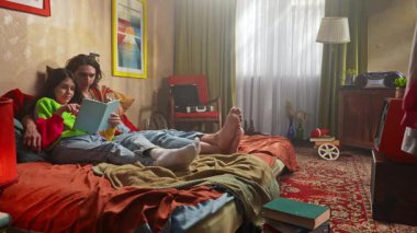 Bir çift, yatak odalarının sıcak, retro atmosferinin ortasında, bir kitaba dalmış, rahat bir şekilde otururlar..