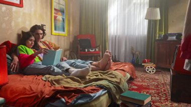 Bir çift, yatak odalarının sıcak, retro atmosferinin ortasında, bir kitaba dalmış, rahat bir şekilde otururlar..