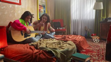 Genç bir çift sıcak bir yatak odasında oturup gitar çalarken sıcak bir atmosfer yaratıyor..