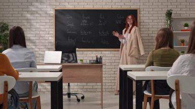 Bir öğretmen öğrencilerin önünde duruyor, modern bir sınıf ortamında tahtada İngilizce gramerini anlatıyor..