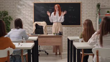 Bir öğretmen nişanlı öğrencilere fiil zamanlarıyla ilgili bir ders veriyor. Sınıf çeşitli zamanları gösteren bir karatahta ile donatılmıştır.