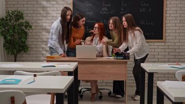 Bir grup öğrenci bir sınıfta dizüstü bilgisayarın etrafında toplanıyor, aktif olarak bir proje üzerinde çalışıyorlar..