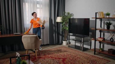 Günlük yaşam tarzı konsepti. Yaşlı yetişkin kadın evde vakit geçiriyor, hafta sonları ev temizliği yapıyor, oturma odasında mobilyaların tozunu alan ve yer düzenleyen bir kadın..