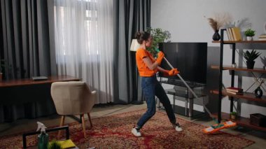 Günlük yaşam tarzı konsepti. Yaşlı yetişkin bir kadın hafta sonları evde vakit geçiriyor. Oturma odasında paspasla halıyı temizleyen, şarkı söyleyen ve dans eden bir kadın yoruluyor..
