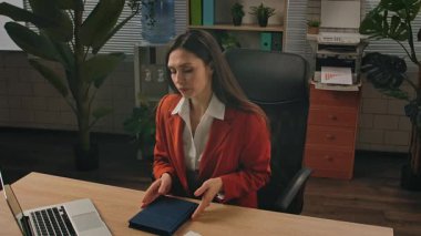 Günlük yaşam tarzı konsepti. Yaşlı, yetişkin bir iş kadını, bitkilerle yeşil ofiste çalışıyor. Masasında oturan, dizüstü bilgisayarı açan, klavyede yazan bir kadın, gün içinde çalışmaya başlıyor..