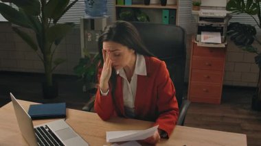 Günlük yaşam tarzı konsepti. Yaşlı, yetişkin iş kadını, bitkilerle yeşil ofiste çalışıyor. Masasında oturan, dizüstü bilgisayarda çalışan, kağıt belgelerini inceleyen, hatalar bulan, hayal kırıklığına uğramış deli ifadesi takınan bir kadın..