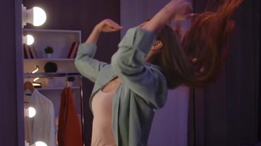 Günlük yaşam tarzı konsepti. Yetişkin bir kadın geceyi evde geçiriyor, aynanın karşısında dikiliyor, kot gömlek giyiyor, saç ve kıyafet tamir ediyor, dışarı çıkmaya hazırlanıyor..