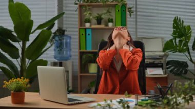 Günlük yaşam tarzı konsepti. Yetişkin bir iş kadını ofiste çalışıyor. Masasında oturan bir kadın dizüstü bilgisayarda çalışıyor. Yorgun bir yüz ifadesi var..