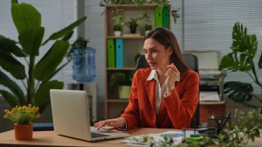 Günlük yaşam tarzı konsepti. Yaşlı, yetişkin bir iş kadını, bitkilerle yeşil ofiste çalışıyor. Masasında oturan bir kadın, harika haberler alıyor. Mutlu kazanma ifadesi. Yavaş çekim.