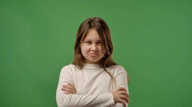 Gençlik duyguları konsepti. Huysuz suratıyla ve çapraz kollarıyla kameraya poz veren genç kız, negatif ifade, krom anahtar yeşil ekran arka plan modelinde izole edilmiş..