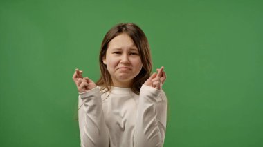 Gençlik duyguları konsepti. Genç kız kameraya poz veriyor, parmaklarını çapraz yapıyor ve beklenen yüz ifadesi, bekleyen yüz ifadesi, krom anahtar yeşil ekran arka plan modelinde izole edilmiş..