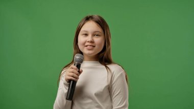 Gençlik duyguları konsepti. Genç kız kameraya poz veriyor, gülümsüyor ve karaoke mikrofonla şarkı söylüyor, pozitif ifade, krom anahtar yeşil ekran arka plan modelinde izole edilmiş..
