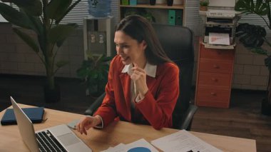 Günlük yaşam tarzı konsepti. Yaşlı, yetişkin bir iş kadını, bitkilerle yeşil ofiste çalışıyor. Masasında oturan bir kadın, harika haberler alıyor. Mutlu kazanma ifadesi. Yavaş çekim.