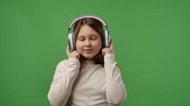 Gençlik duyguları konsepti. Kameraya poz veren genç bir kız kulaklıkla müzik dinliyor, dans ediyor, pozitif ifade ediyor, krom anahtar yeşil ekran arka plan modelinde izole edilmiş. Yavaş çekim