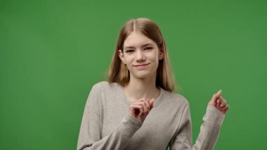 Gençlik duyguları konsepti. Genç kız kameraya poz veriyor, gülümsüyor, komik dans ediyor, pozitif ifade ediyor, yeşil ekran arka plan modelinde izole edilmiş. Yavaş çekim