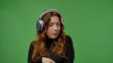 Gençlik duyguları konsepti. Kameraya poz veren genç bir kız kulaklıkla müzik dinliyor, dans ediyor, pozitif ifade ediyor, krom anahtar yeşil ekran arka plan modelinde izole edilmiş. Yavaş çekim