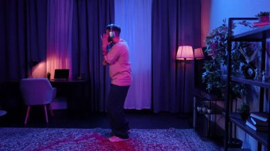 Kulaklıklı genç bir adam parlak bir odada müzik dinliyor ve enerjik bir şekilde hip hop yapıyor. Yavaş Hareket