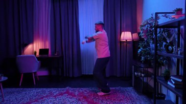 Parlak renkli ışıklandırmalı şık bir odada hip hop yapan bir adam enerjik bir atmosfer yaratıyor. Yavaş Hareket