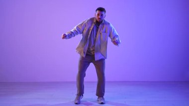 Sıradan takım elbiseli bir adam, sahnede mor ışıkla hip hop yapıyor, enerjik hareketlerini ve tarzını sergiliyor. Yavaş Hareket