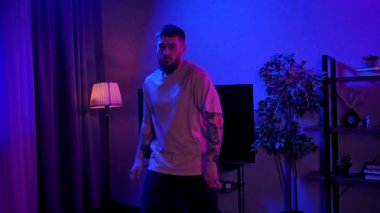 Canlı, neon ışıklı, dinamik mor ve mavi ışıklarla dolu bir odada hip hop yapan bir adam. Yavaş Hareket