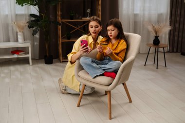 Kadın ve genç kız birlikte oturur, rahat bir oturma odasında telefon ve kredi kartıyla online alışveriş yaparlar..