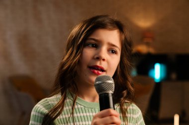 Genç bir kız tutkuyla mikrofona şarkı söylüyor. Sıcak bir oda ortamında..