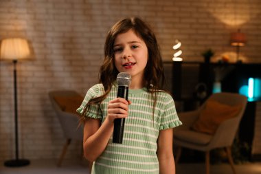 Genç bir kız tutkuyla mikrofona şarkı söylüyor. Sıcak bir oda ortamında..