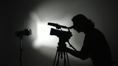 Bir stüdyo ortamında çekim yapan bir kameraman silueti film yapımının yaratıcı sürecini vurguluyor..