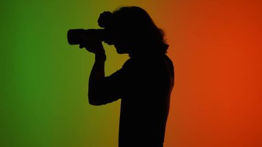 Canlı yeşil ve turuncu arkaplanı olan büyüleyici bir fotoğrafçı silueti çarpıcı bir görsel karşıtlık yaratır.