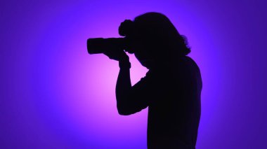 Bir fotoğrafçının silüeti canlı mor bir arkaplan karşısında anları yakalıyor, fotoğrafçılığın yaratıcılığını ve tutkusunu vurguluyor..