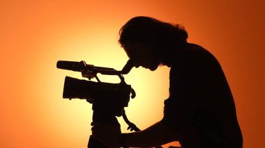 Canlı bir günbatımına karşı silueti olan bir kameraman, ekipman ve sanatsal odağı vurguluyor..