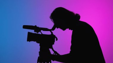 Bir kameraman, gradyan ışıklandırmalı bir stüdyo ortamında çekim yaparken siluette yakalanır..