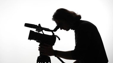 Profesyonel bir kamera kullanan bir kameramanın silueti, film yapma sanatını ön plana çıkarıyor..