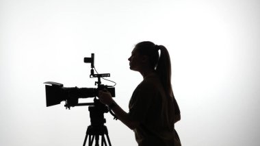 Profesyonel video kamera kullanan bir kadının silüeti, film yapma sanatını ön plana çıkarıyor..